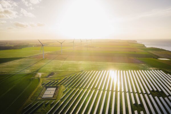 Sun rising, horizon, wind turbines, solar pv panels in field.