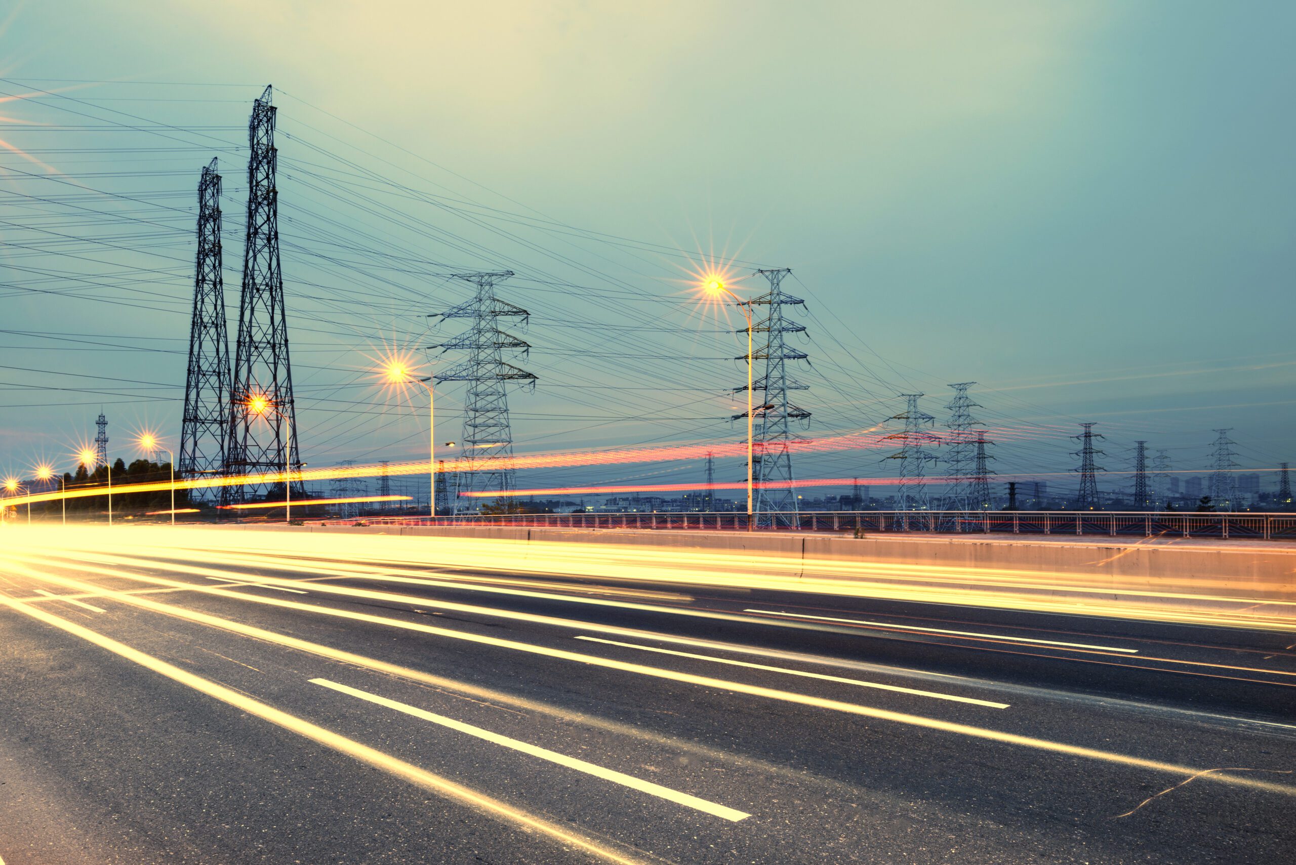 Electricity pylons near a road at twilight.