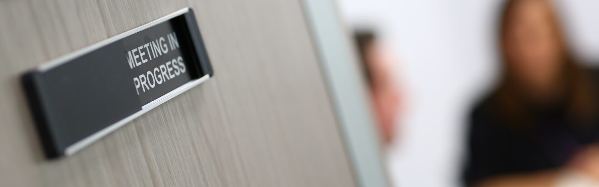 A door with a "meeting in progress"-sign. (Source: Adobe Stock.)