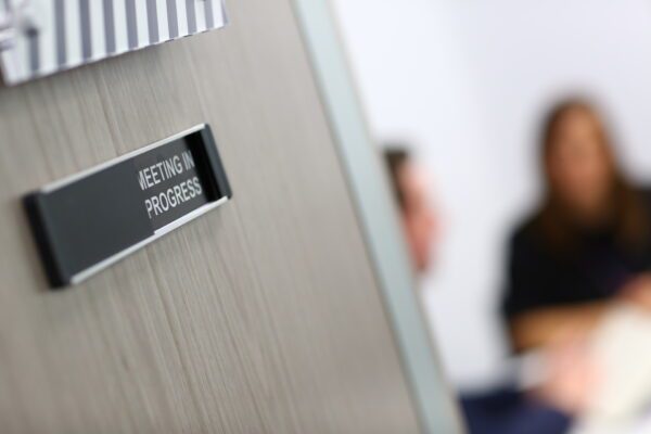Feature image A door with a "meeting in progress"-sign. (Source: Adobe Stock.)