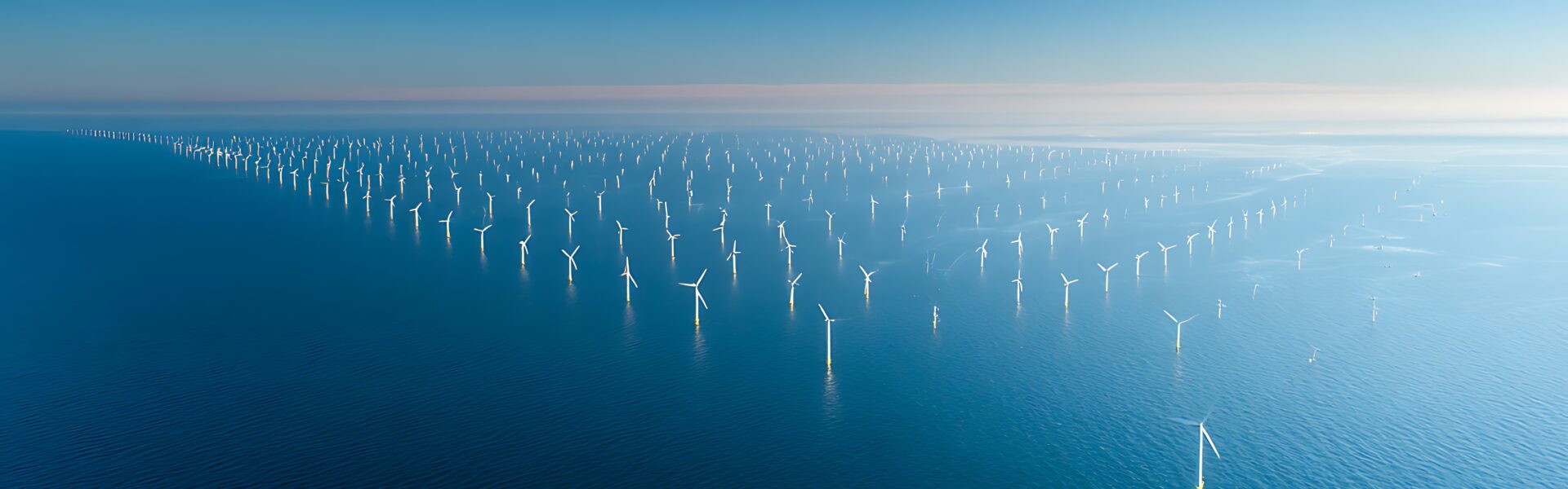 Aerial view of a large offshore wind farm with rows of turbines in the blue ocean water under clear sky